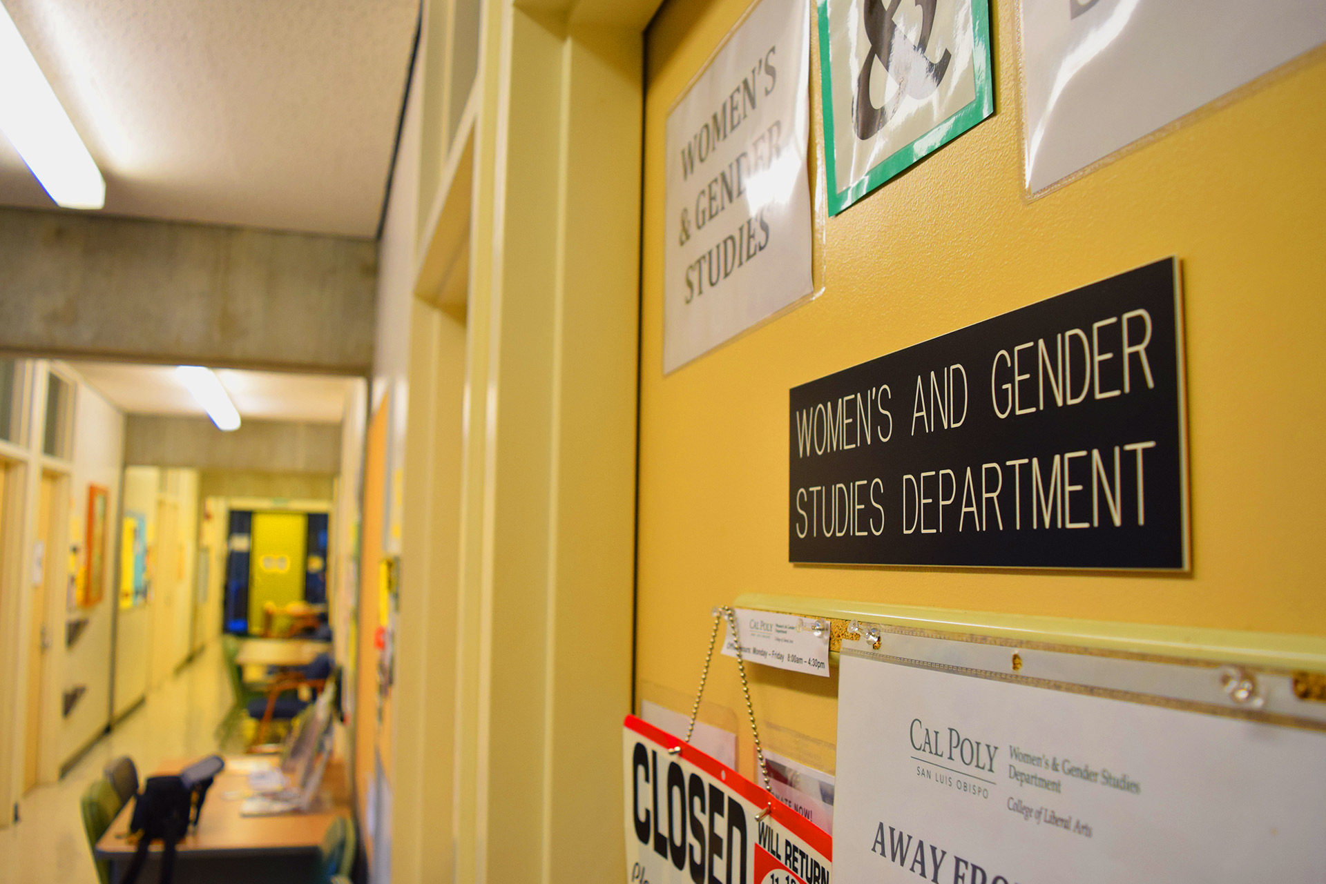 Contrary to the recreational culture of the university, the academic world of Cal Poly was slower to gain acceptance of LGBTQ+ studies and issues. The Women and Gender Studies minor was introduced in 1990, and a Queer Studies minor debuted in 2017. Shown here is the titular office in the WGS Department’s hallway deep in Building 47 (known as the ‘Maze’ for good reason), belonging to Department Coordinator K. Weldon.  Photo Credit: Katelyn Biddle