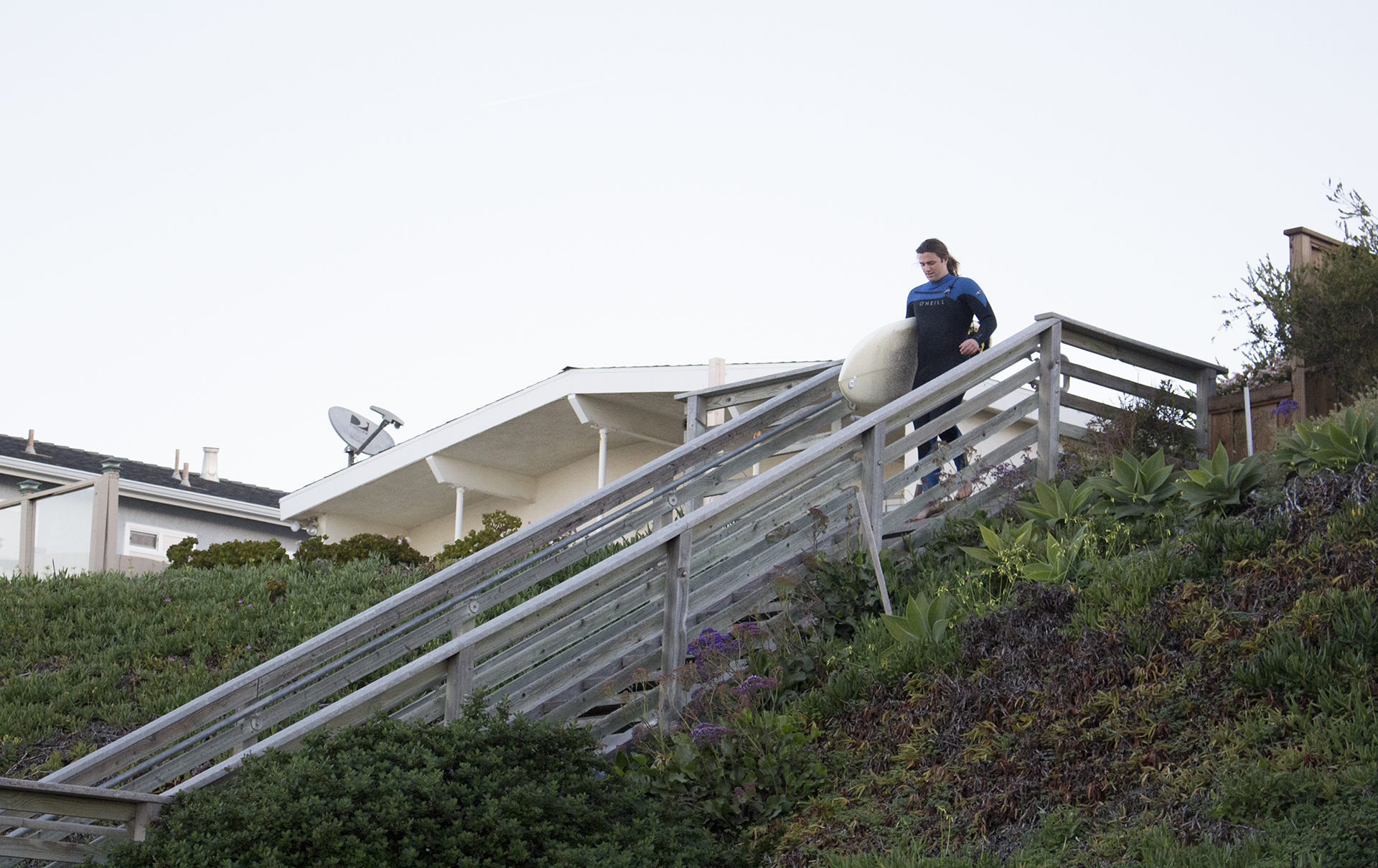 <strong>Catching up</strong> - Cal Poly liberal studies junior Quaid Tatlow is running down the stairs a second time after running back to his car from the beach. “I couldn’t decide which board to use,” he said. Tatlow, already behind the group, switched boards to adjust for the wind and waves at Studios in Cayucos.